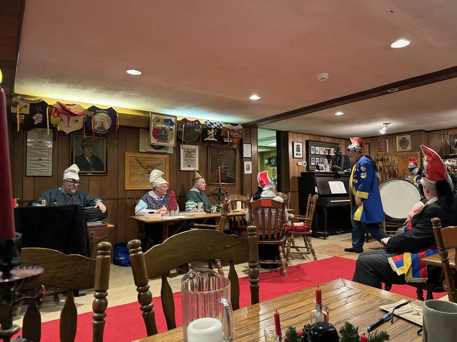 Sassen der Newarka an der Tafel in der Trutze Passaica der Fuchsbau — getäfelte Wände mit Wappen, roter Läufer, Klavier und Trommel
